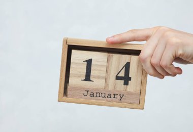 Kadının elinde tahta blok takvimi var. Tarihi 14 Ocak, beyaz beton arka planda.
