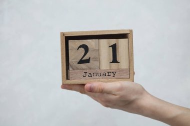 Kadının elinde tahta blok takvimi var. Tarihi 21 Ocak, beyaz beton arka planda.