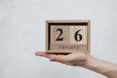 26 Ocak tarihli tahta blok takvimi beyaz beton arka planda bir kadının elinde.