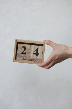 24 Ocak tarihli tahta blok takvimi beyaz beton arka planda bir kadının elinde.