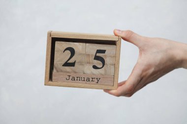 25 Ocak tarihli tahta blok takvimi beyaz beton arka planda bir kadının elinde.