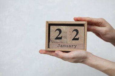 22 Ocak tarihli tahta blok takvimi beyaz beton arka planda bir kadının elinde.