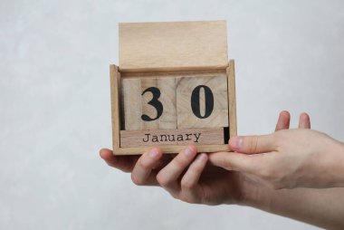 Kadının elinde tahta blok takvimi var. Tarihi 30 Ocak, beyaz beton arka planda.