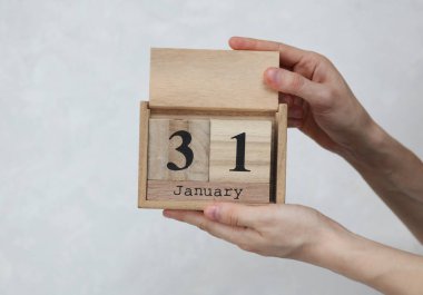 Kadının elinde tahta blok takvimi var. Tarihi 31 Ocak, beyaz beton arka planda.