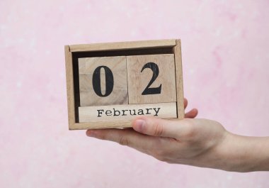 Kadının elinde tahta blok takvimi var. Tarihi 02 Şubat, pembe beton arka plan.