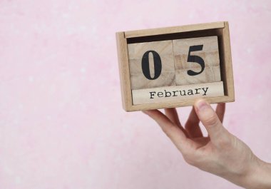 Kadının elinde tahta blok takvimi var. Pembe beton arka planda Şubat 05 tarihli.