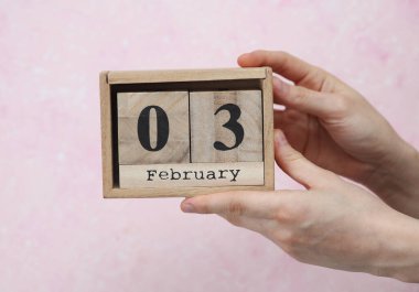 Kadının elinde tahta blok takvimi var. Tarih Şubat 03, pembe beton arka plan.