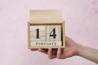 Kadının elinde tahta blok takvimi var. Tarihi 14 Şubat, pembe beton arka plan.