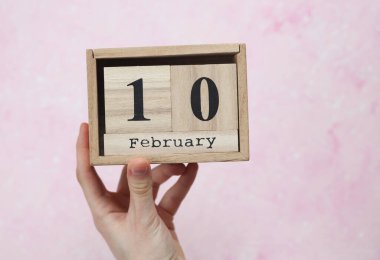 Kadının elinde tahta blok takvimi var. 10 Şubat 'ta pembe beton arka planda.