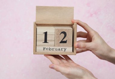 Kadının elinde, üzerinde 12 Şubat tarihli pembe beton zemin olan tahta blok takvimi var.