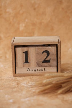 12 Ağustos tarihli tahta blok takvimi ve bej beton arka planda buğday başakları