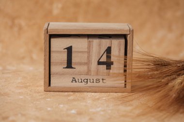 14 Ağustos tarihli ahşap blok takvimi ve bej beton arka planda buğday başakları