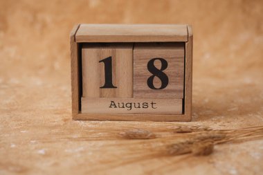 18 Ağustos tarihli tahta blok takvimi ve bej beton arka planda buğday başakları