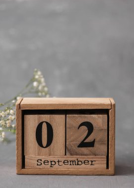 Tahta takvim, tarihi 02 Eylül ve gri çimento arka planda çigila çiçekleri.