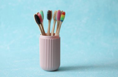 Mavi beton arka planda plastik bir organizatör çantasında bir dizi eko bambu diş fırçası.