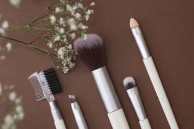 Kahverengi arka planda makyaj fırçaları ve çigila çiçekleri.