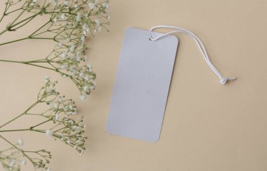 Beyaz boş fiyat etiketi ve bej arka planda çingene çiçekleri