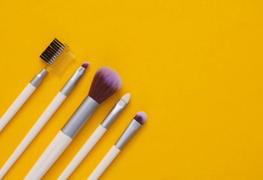 Sarı arka planda makyaj fırçaları. Boşluğu kopyala