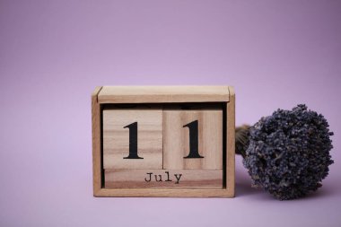 11 Temmuz tarihli ahşap blok takvimi ve bir buket kuru lavanta çiçeği.