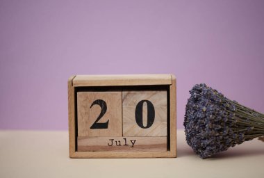 20 Temmuz tarihli ahşap blok takvimi ve bir buket kuru lavanta çiçeği.