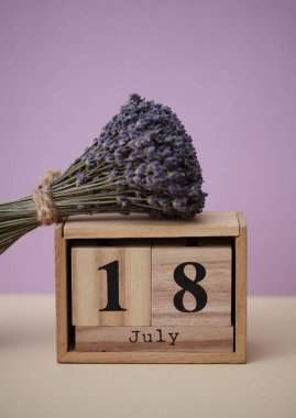 18 Temmuz tarihli tahta blok takvimi ve bir buket kuru lavanta çiçeği.