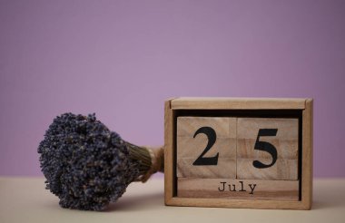 Tahta blok takviminde 25 Temmuz tarihi ve bir buket kuru lavanta çiçeği var.