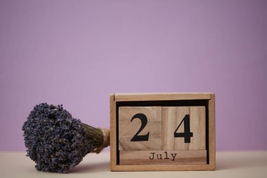 24 Temmuz tarihli ahşap blok takvimi ve bir buket kuru lavanta çiçeği.