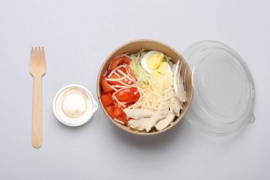 Sezar salatası gri arka planda tek kullanımlık karton bir kutuda.