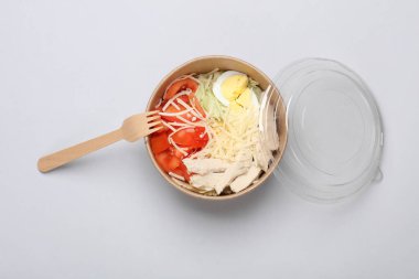 Sezar salatası gri arka planda tek kullanımlık karton bir kutuda.