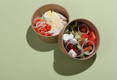 Yeşil arka planda tek kullanımlık karton kaplarda Yunan ve Sezar salatası