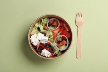 Yeşil arka planda tahta kaşıkla tek kullanımlık konteynırda Yunan salatası. Eko kavramı