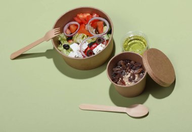 Tek kullanımlık yiyecek kapları, Yunan salatası ve yeşil arka planda kuru üzümlü yulaf ezmesi. Paket yemek.