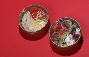 Kırmızı arka planda tek kullanımlık karton kaplarda Yunan ve Sezar salatası