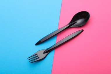 Pembe arka planda siyah plastik kaşık ve çatal