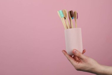 Elinde pembe arka planda bambu diş fırçası olan plastik organizatör çantası.