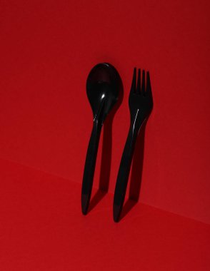 Kırmızı arka planda siyah plastik kaşık ve çatal, gölgeli. Yaratıcı yerleşim