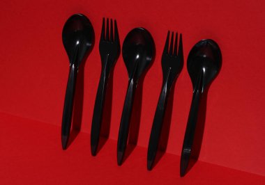 Siyah plastik kaşıklar ve çatallar kırmızı arka planda gölgeli. Yaratıcı yerleşim