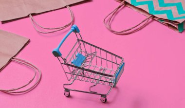 Pembe arka planda alışveriş arabası ve kese kağıdı olan bir model. Mutlu müşteri konsepti. İnternet alışverişi. İnternetteki mağaza. Tüketim, yaşam tarzı 