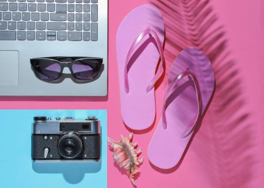 Yaz tatili. Yaz tatili dinlenme zamanı. Laptop ve plaj aksesuarları pembe mavi arka planda, palmiye yaprağı gölgesinde. Stüdyo kısa. Plaj objesi. Üst görünüm