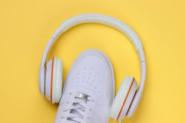Sarı arka planda kulaklık takan beyaz spor ayakkabılar. Modern yaratıcı. Sıradan tasarım. Müzik konsepti. Düz yatış, minimum.