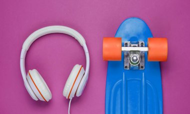 Hippi kıyafeti. Mor arka planda kulaklıkları olan kaykay. Yaratıcı moda minimalizmi. Modaya uygun, modaya uygun. Asgari yaz eğlencesi. Müzik konsepti