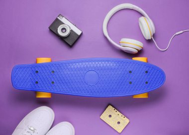 Hippi kıyafeti. Kulaklıklı kaykay, spor ayakkabısı, retro kamera, mor arka planda ses kaseti. Yaratıcı moda minimalizmi. Modaya uygun, modaya uygun. Asgari yaz eğlencesi. Müzik konsepti. Üst görünüm