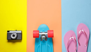 Hippi kıyafeti. Retro kameralı kaykay, renkli arka planda parmak arası terlik. Yaratıcı moda minimalizmi. Modaya uygun, modaya uygun. Asgari yaz eğlencesi. Müzik konsepti. Üst görünüm