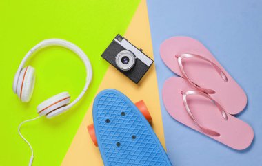 Hippi kıyafeti. Kulaklıklı kaykay, parmak arası terlik, renkli arka planda retro kamera. Yaratıcı moda minimalizmi. Eski moda 80 'ler tarzı. Asgari yaz eğlencesi. Müzik konsepti. Üst görünüm