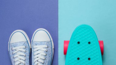 Mor mavi arka planda hippi spor ayakkabıları ve kaykay üstü görünümü. Minimalizm moda kavramı.