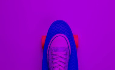 Hipster spor ayakkabıları kaykayın üstünde üstten mor neon ışıkta. Minimalizm yaşam tarzı kavramı