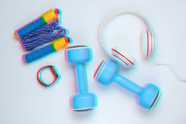 Dambıllar, akıllı bilezikler, kulaklıklar, beyaz arka planda ip atlama. Minimalist spor konsepti. Arıza etkisi. Üst görünüm.