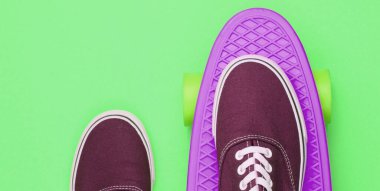 Hipster spor ayakkabıları kaykayın üstünde üstten yeşil arka planda. Minimalizm moda kavramı