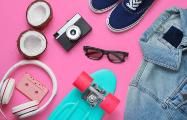 Hippi kıyafeti. Kulaklıklı kaykay, kot ceket, ses kaseti, retro kamera, pembe arka planda hindistan cevizi ve spor ayakkabı. Yaratıcı moda minimalizmi. Asgari yaz eğlencesi. 80 'ler. Üst görünüm