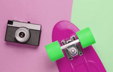 Renkli pastel arka planda kaykay ve film kamerası olan bir Retro seti. Stüdyo çekimi. Gençlik yaşam tarzı. 80 'ler. Üst görünüm